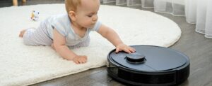 Cute little baby boy looking with interest on robot vacuum cleaner