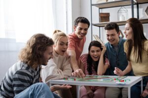 KYIV, UKRAINE - JANUARY 27, 2020: excited young friends playing monopoly game at home
